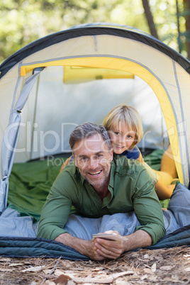Father and son with mobile phone resting in tent at campsite