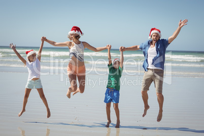 Cheerful family wearing Santa hat while jumping at beach