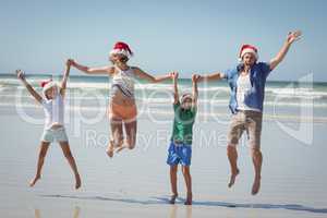 Cheerful family wearing Santa hat while jumping at beach