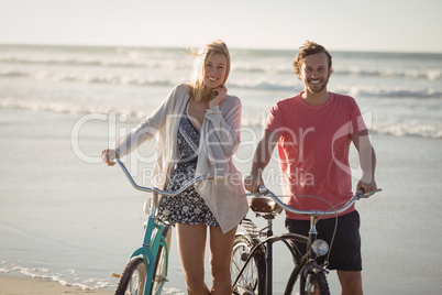 Portrait of smiling couple with bicycles standing at beach