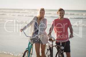 Portrait of smiling couple with bicycles standing at beach