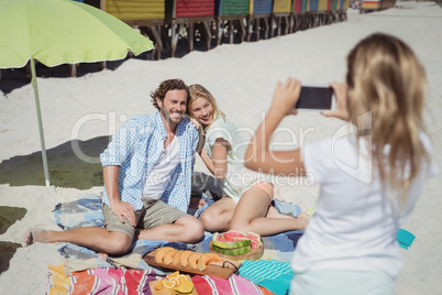 Parents smiling while daughter photographing them at beach