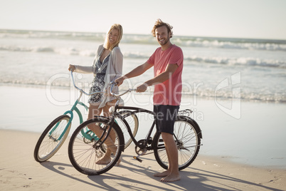 Portrait of young couple with bicycles standing at beach