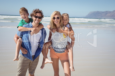 Portrait of smiling parents piggybacking their children at beach