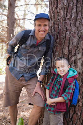 Portrait of happy father and son leaning on tree trunk