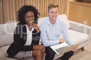 Portrait smiling executives sitting with laptop on sofa