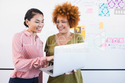 Smiling businesswomen using laptop white standing against whiteboard