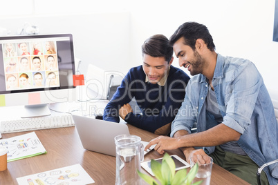Smiling businessmen using laptop at desk in office