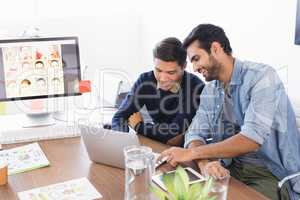 Smiling businessmen using laptop at desk in office