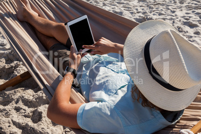 Man relaxing on hammock and using digital tablet on the beach