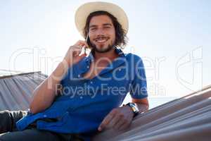Portrait of smiling man talking on mobile phone while relaxing at beach