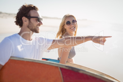Happy man with woman gesturing while carrying sunrfboard at beach