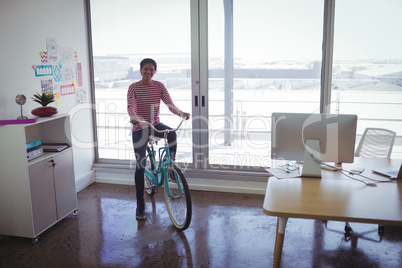 Smiling businesswoman riding bicycle in creative office