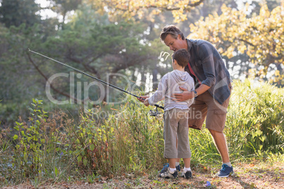 Father teaching boy fishing in forest