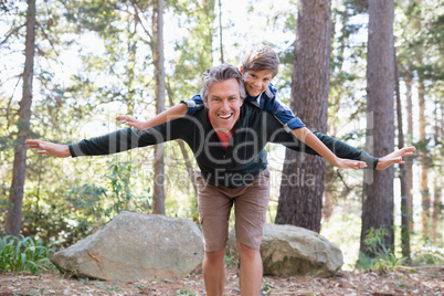 Cheerful father piggybacking son while hiking in forest