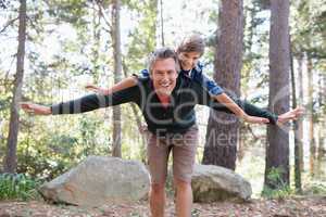 Cheerful father piggybacking son while hiking in forest
