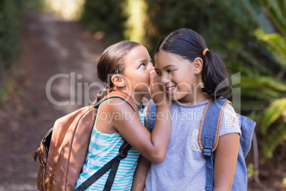 Girl whispering to friend at natural parkland