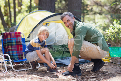 Smiling father and son tying shoelace by tent at campsite