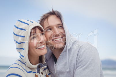 Smiling couple wearing hooded sweater while looking away