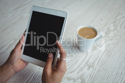Hands of businesswoman holding holding digital tablet by coffee cup on table