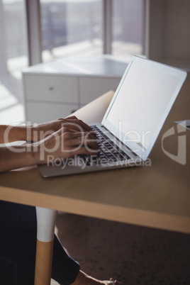 Businesswoman using laptop on wooden desk in office