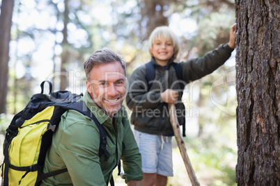 Smiling father and son carrying backpacks while hiking in forest