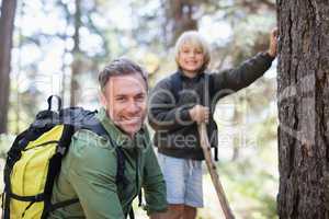 Smiling father and son carrying backpacks while hiking in forest
