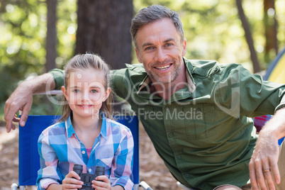 Happy father and daughter sitting at campsite in forest