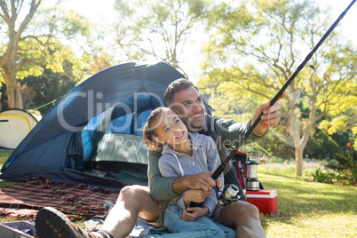 Father and daughter holding a fishing rod outside the tent