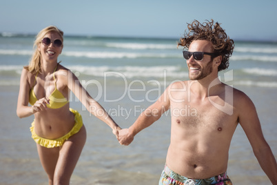 Happy couple holding hands while running at beach