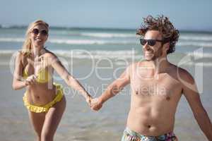 Happy couple holding hands while running at beach