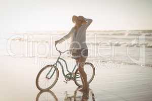 Full length of woman standing by bicycle on shore at beach