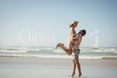 Side view of man lifting woman at beach