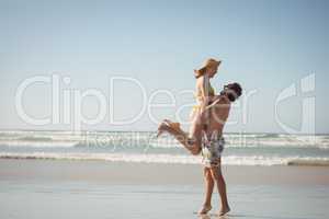 Side view of man lifting woman at beach