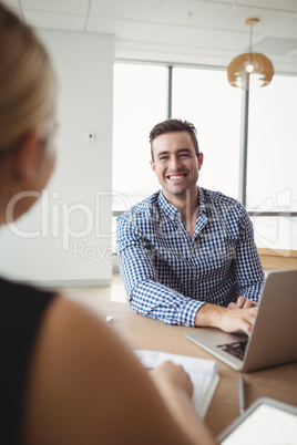 Executive interacting with colleague while working on computer at desk
