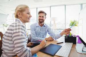 Smiling executives discussing over personal computer at desk