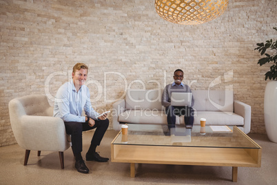 Portrait of smiling executives using digital tablet and laptop