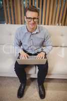 Portrait of smiling executive sitting on sofa and using laptop