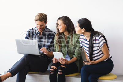 Businesswomen looking at businessman while sitting against wall