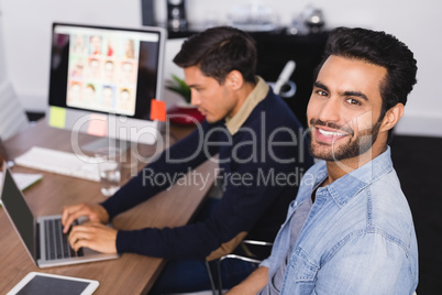 Portrait of smiling businessman with colleague at desk