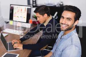 Portrait of smiling businessman with colleague at desk