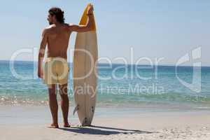 Surfer with surfboard looking at sea from the beach