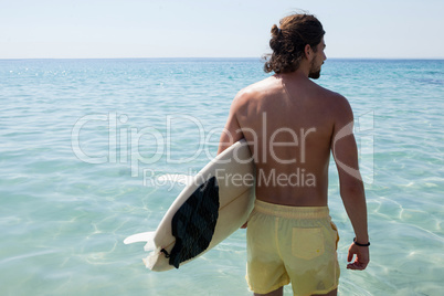 Surfer with surfboard looking at sea from the beach