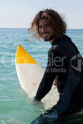 Smiling surfer sitting on surfboard at seacoast