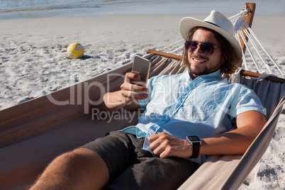 Man relaxing on hammock and using mobile phone on the beach