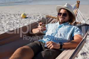 Man relaxing on hammock and using mobile phone on the beach