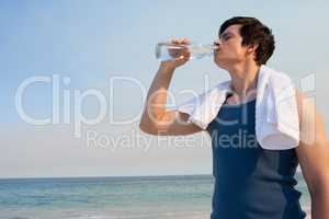 Young man drinking water from bottle at beach