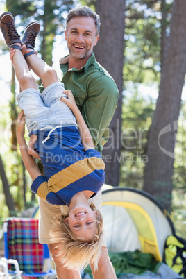 Cheerful father holding son upside down at campsite