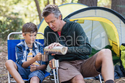Father pouring drink in cup for son in forest