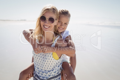 Happy mother piggybacking her daughter at beach